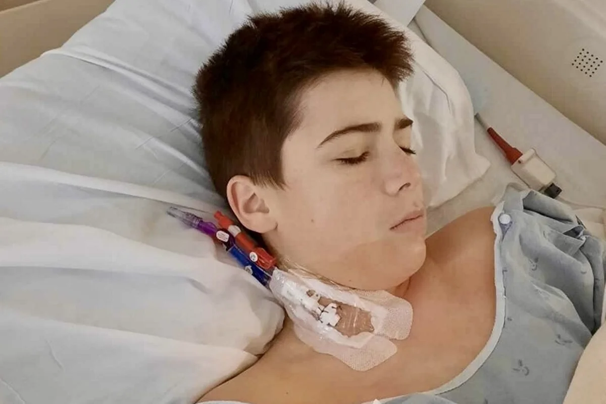 Foto colorida de garoto deitando em uma cama de hospital, com tubos conectados no seu pescoço - Metrópoles.
