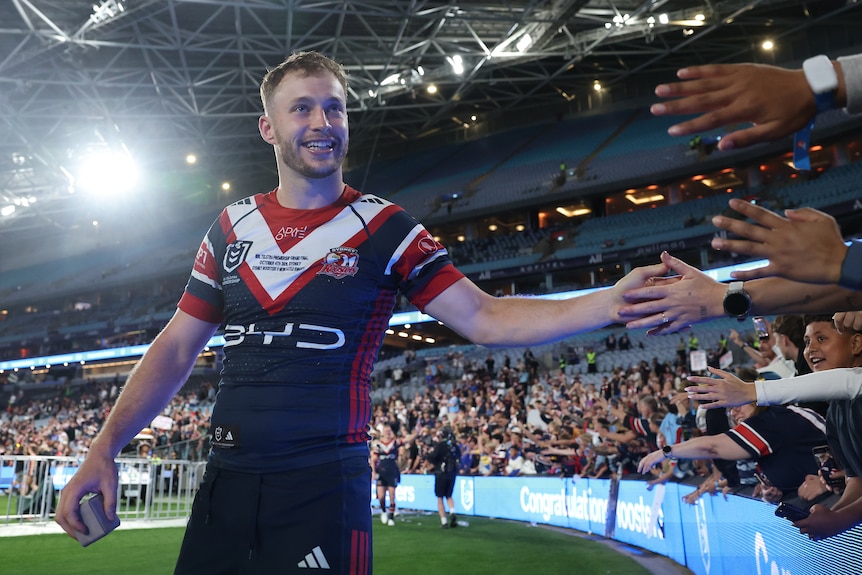 A smiling Sydney Roosters NRL player reaches his hand out to high-five fans after a grand final win.