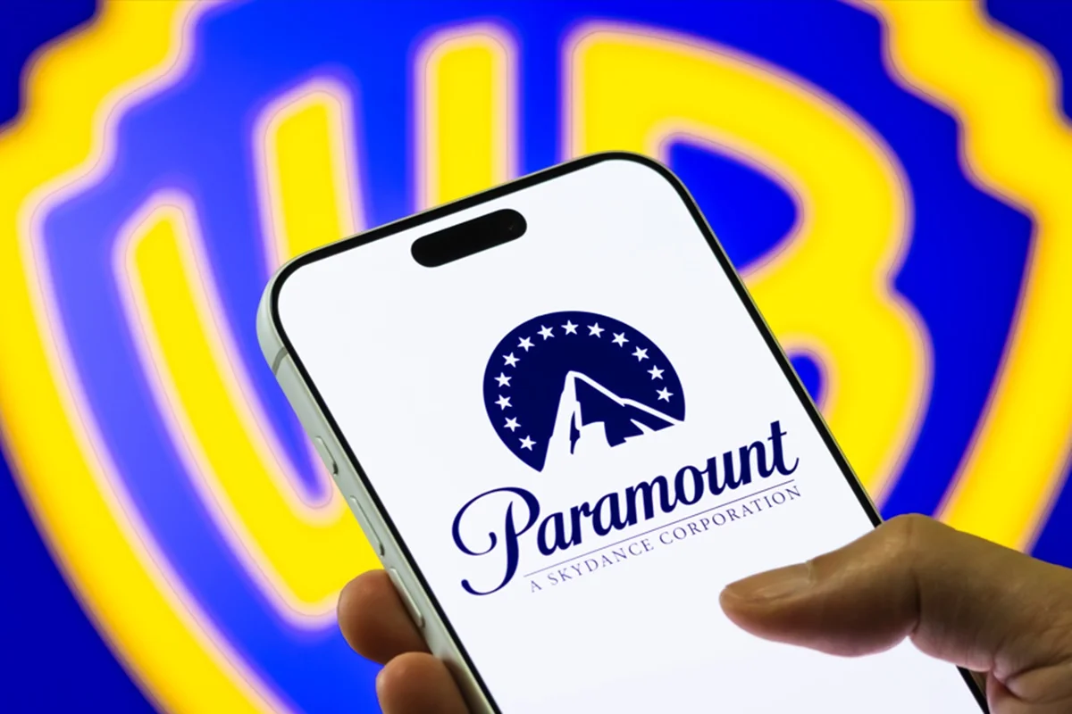 Imagem de celular exibindo a logomarca da Paramount e, ao fundo, a imagem do logotipo da Warner - Metrópoles
