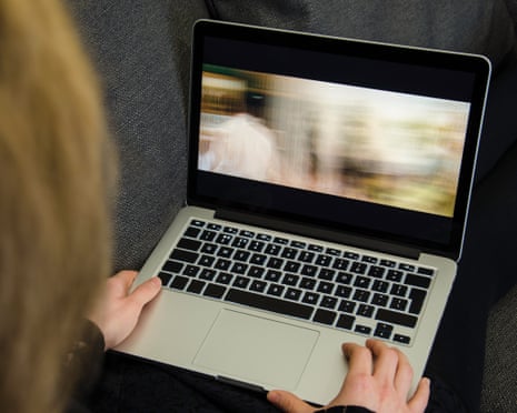 A woman watches a blurred, colourful film on a laptop screen resting on her lap