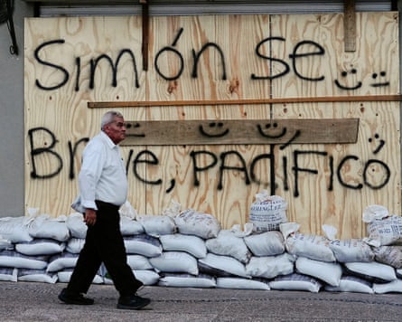 A man walks past a boarded-up business in Puerto Vallarta bearing the message ‘Simon, be brief, be peaceful’
